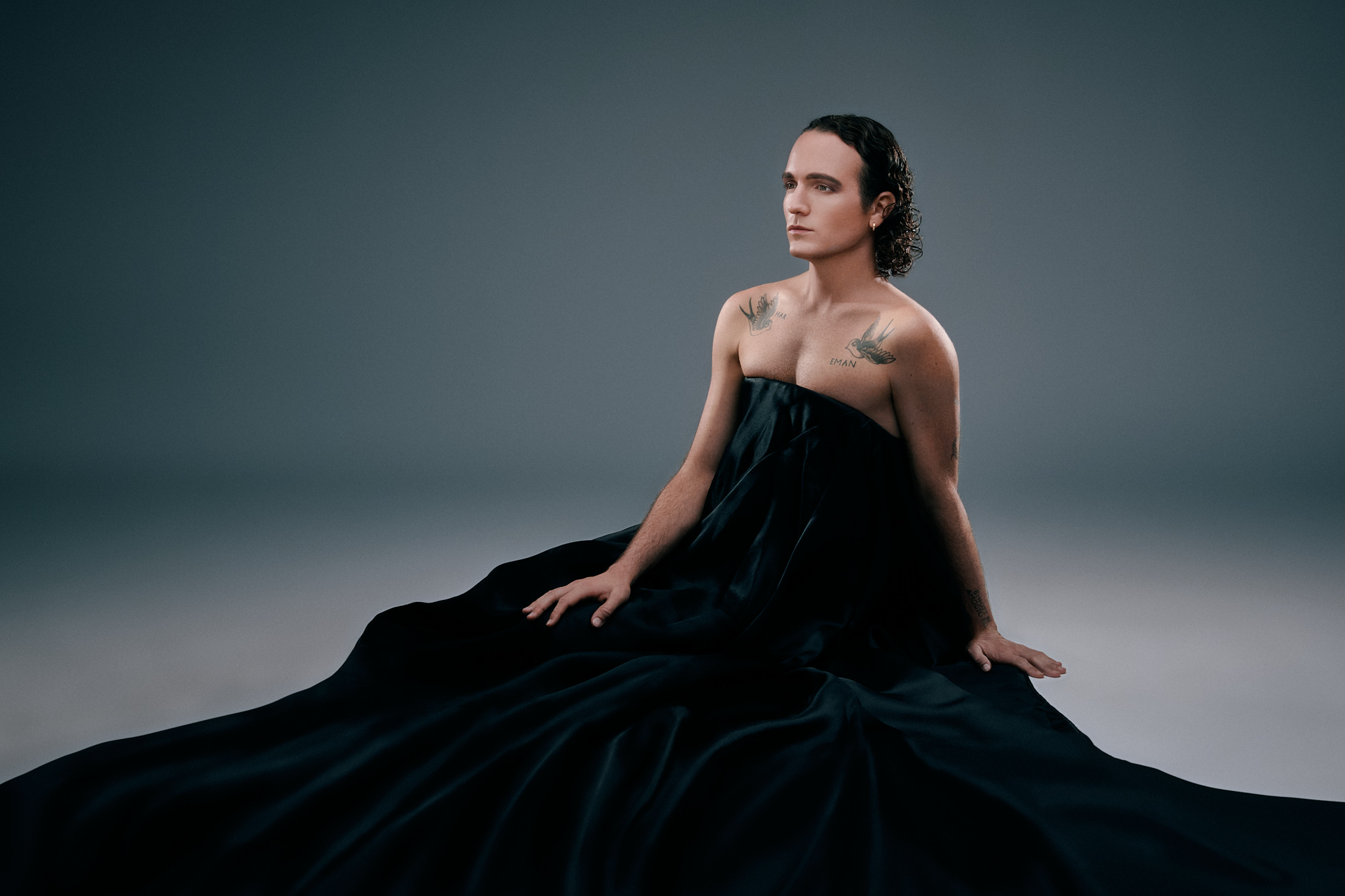 A young man wearing a long dress is sitting on the floor (Arnaud Gimbert)